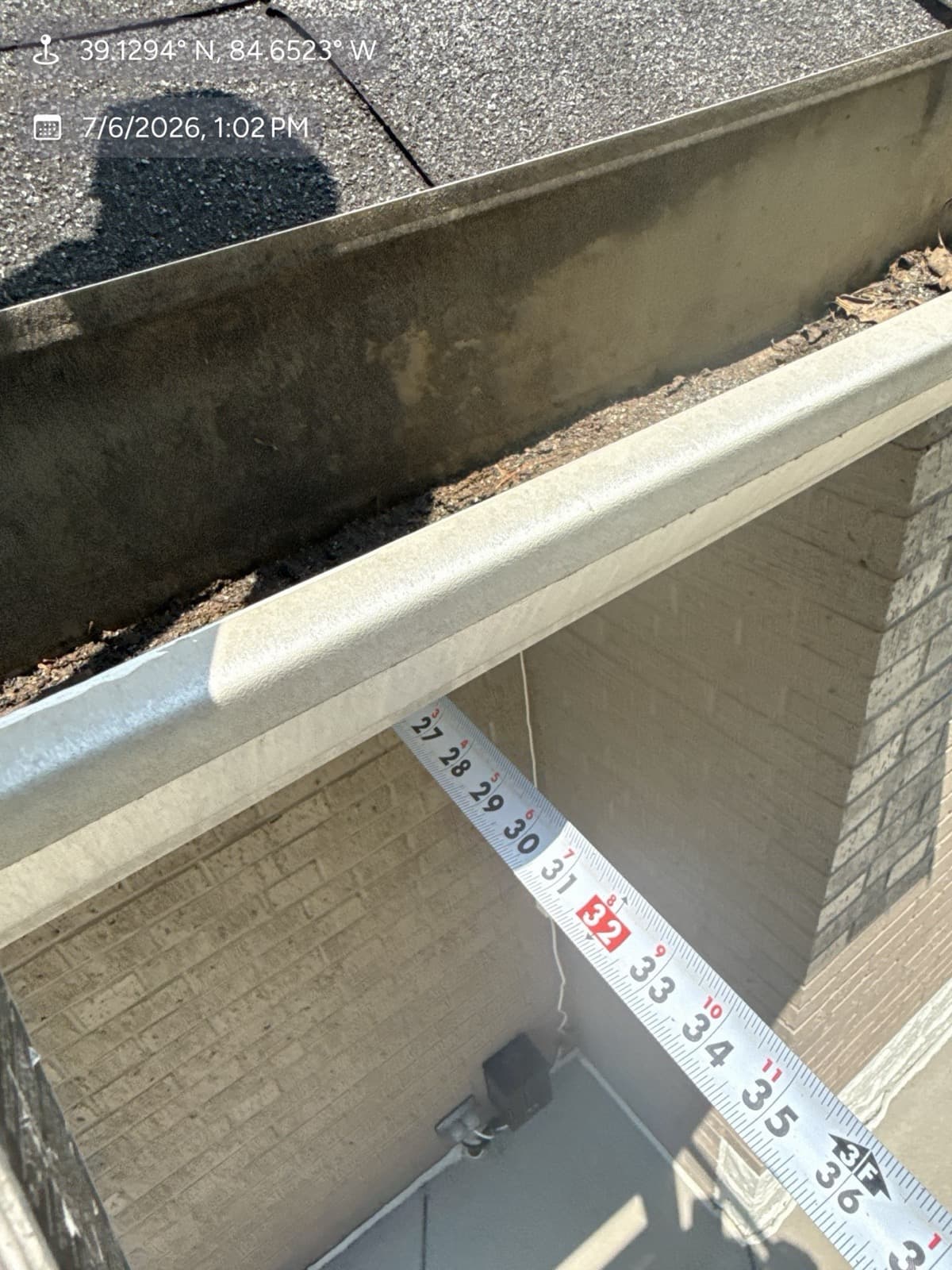 Tape measure documenting hail dents in a gutter during a roof inspection