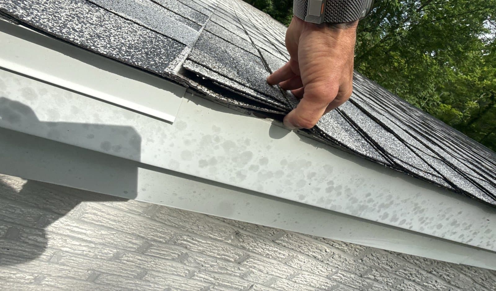 Roofer lifting failing shingles at the roof edge during a storm damage inspection in Cincinnati